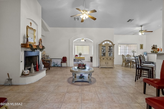 living area with a fireplace with raised hearth, visible vents, lofted ceiling, and a ceiling fan