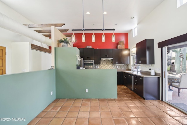 kitchen featuring a towering ceiling, oven, dishwashing machine, pendant lighting, and backsplash