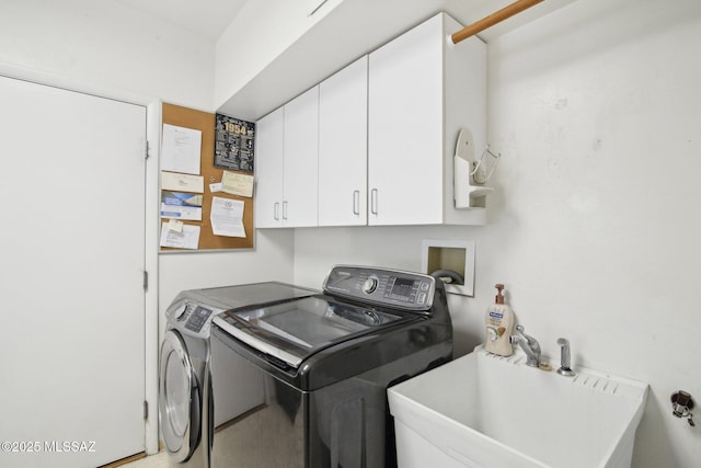 clothes washing area with washing machine and dryer, cabinets, and sink