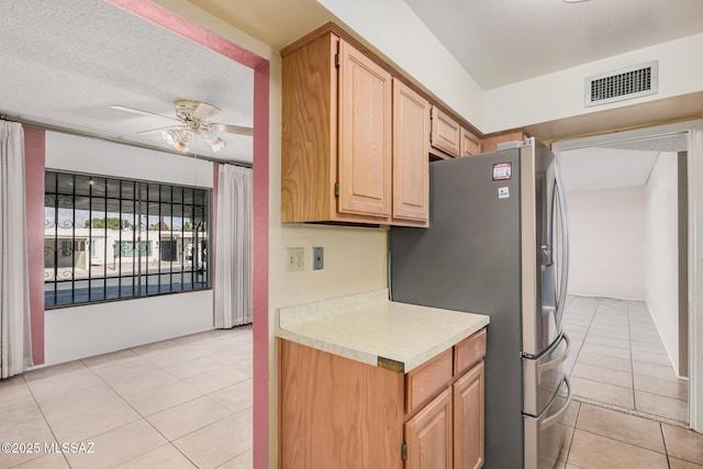 kitchen with stainless steel fridge with ice dispenser, light tile patterned floors, ceiling fan, light brown cabinets, and a textured ceiling