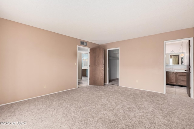 unfurnished bedroom featuring ensuite bath, light colored carpet, a closet, and a spacious closet