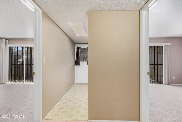 hallway with a textured ceiling and light colored carpet