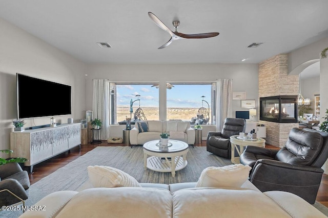 living area with ceiling fan, wood finished floors, a multi sided fireplace, and visible vents