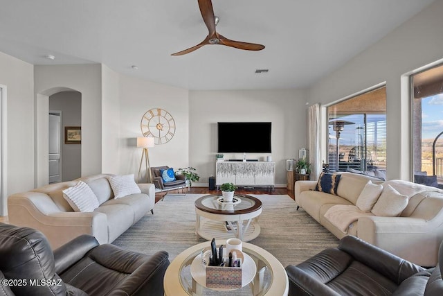 living area with ceiling fan, arched walkways, wood finished floors, visible vents, and baseboards