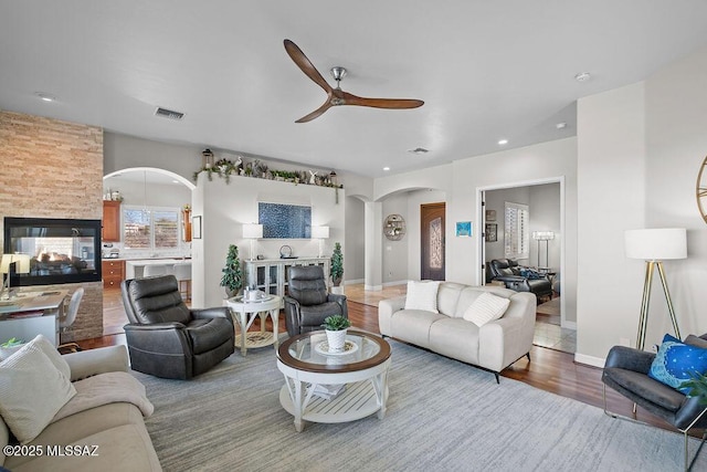 living area featuring visible vents, arched walkways, ceiling fan, wood finished floors, and a multi sided fireplace