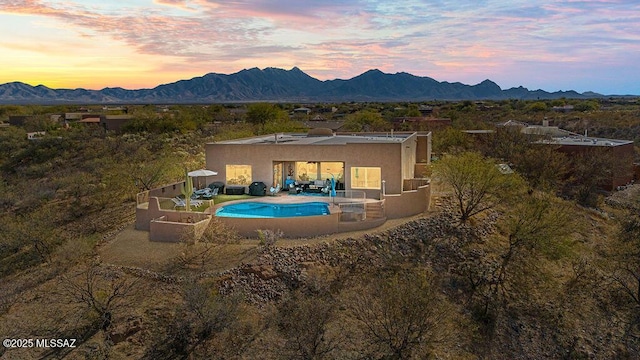 pool at dusk with an outdoor pool, a mountain view, and a patio