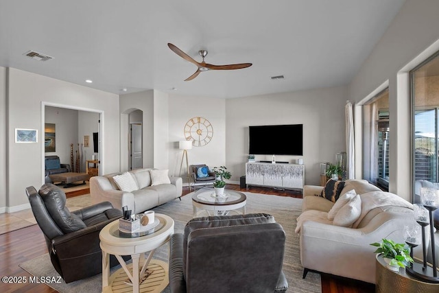 living room with arched walkways, visible vents, ceiling fan, wood finished floors, and baseboards