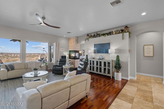 living area with arched walkways, visible vents, ceiling fan, wood finished floors, and baseboards