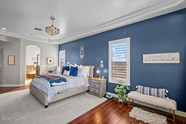 bedroom featuring baseboards, visible vents, arched walkways, ensuite bath, and wood finished floors