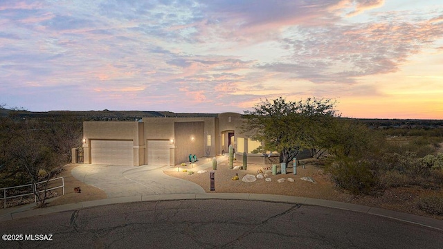 pueblo revival-style home with concrete driveway, an attached garage, and stucco siding