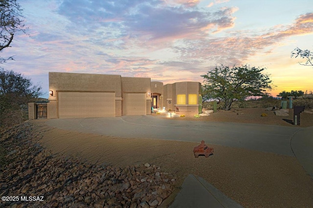 pueblo revival-style home featuring concrete driveway, an attached garage, and stucco siding