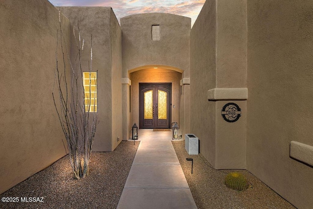 exterior entry at dusk with stucco siding and french doors