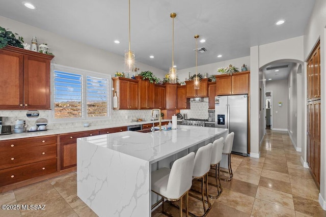 kitchen featuring a center island with sink, visible vents, arched walkways, brown cabinets, and stainless steel refrigerator with ice dispenser