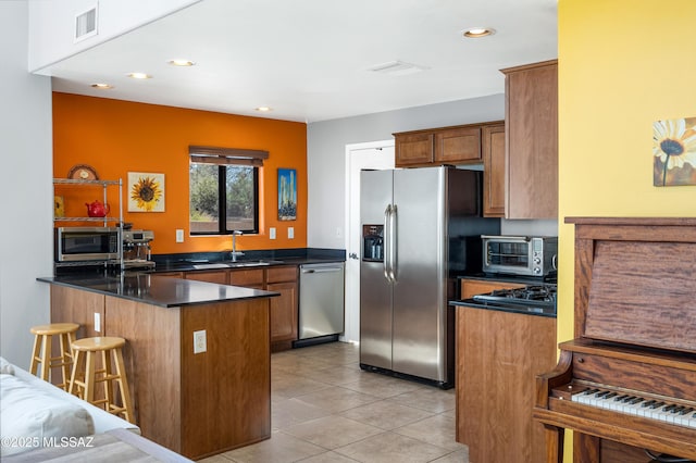 kitchen featuring light tile patterned floors, kitchen peninsula, stainless steel appliances, a breakfast bar, and sink