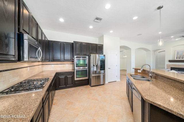 kitchen with appliances with stainless steel finishes, tasteful backsplash, pendant lighting, light stone counters, and sink