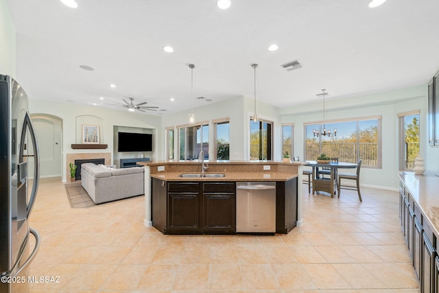 kitchen with ceiling fan with notable chandelier, decorative light fixtures, stainless steel appliances, an island with sink, and sink