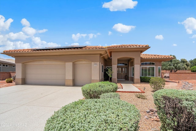 mediterranean / spanish home featuring concrete driveway, solar panels, a tiled roof, an attached garage, and stucco siding