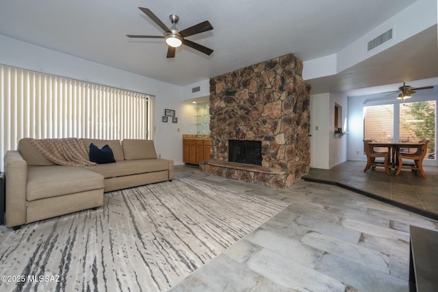 living room with ceiling fan and a stone fireplace