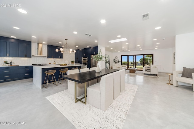 kitchen featuring a kitchen island, wall chimney exhaust hood, blue cabinetry, and a kitchen bar