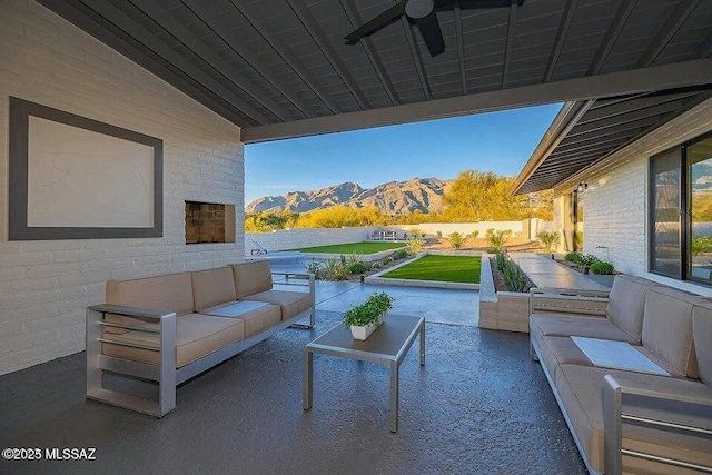 view of patio featuring a mountain view, an outdoor living space with a fireplace, and ceiling fan