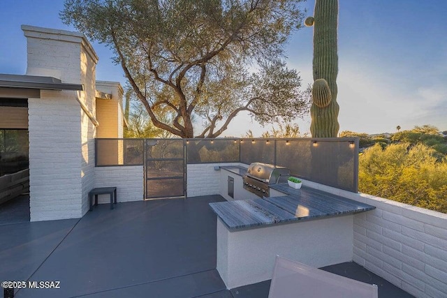 patio terrace at dusk featuring area for grilling and exterior kitchen