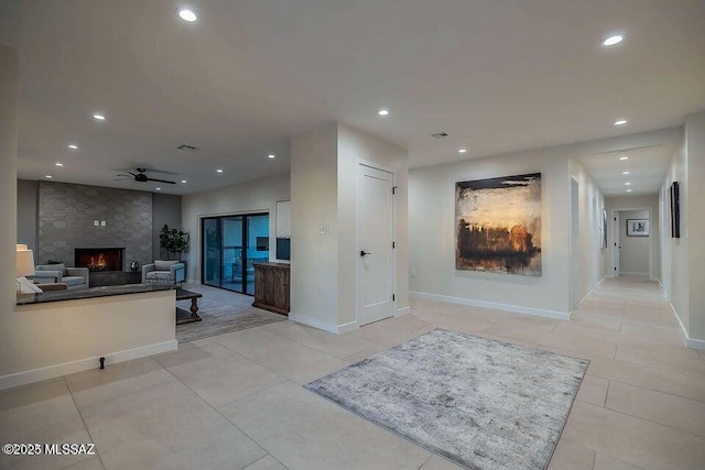 kitchen featuring ceiling fan, a stone fireplace, and light tile patterned floors