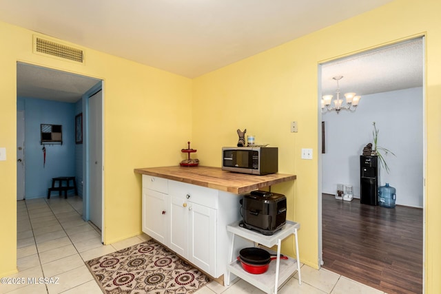 kitchen featuring white cabinetry, light tile patterned floors, wood counters, hanging light fixtures, and a notable chandelier