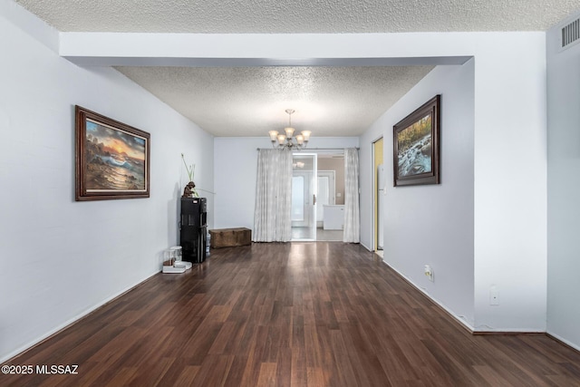 unfurnished living room with dark hardwood / wood-style flooring, a textured ceiling, and a chandelier