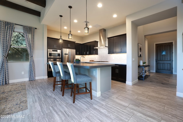 kitchen featuring stainless steel appliances, decorative backsplash, a kitchen island with sink, hanging light fixtures, and wall chimney range hood