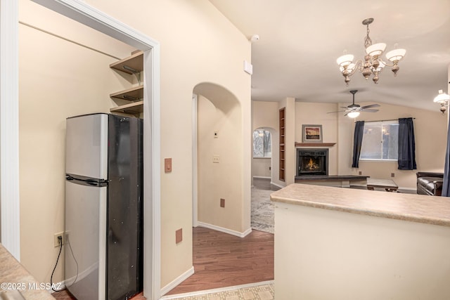 kitchen with vaulted ceiling, ceiling fan with notable chandelier, pendant lighting, stainless steel refrigerator, and light hardwood / wood-style flooring