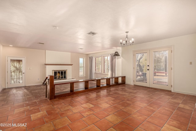 unfurnished living room with an inviting chandelier, tile patterned flooring, and french doors