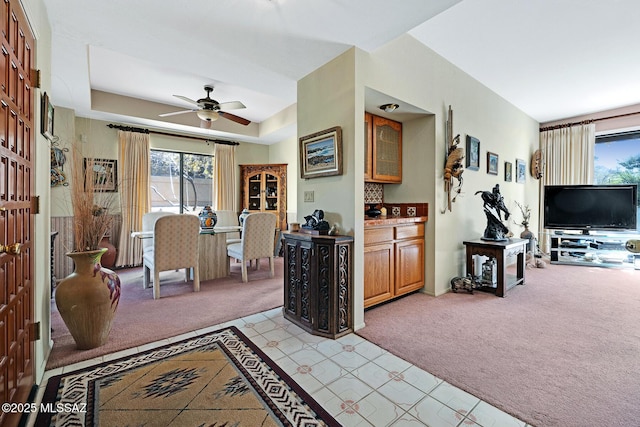 carpeted living room with ceiling fan, a raised ceiling, and a healthy amount of sunlight