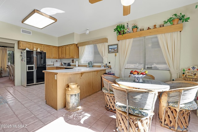 kitchen with light tile patterned floors, ceiling fan, kitchen peninsula, and black fridge