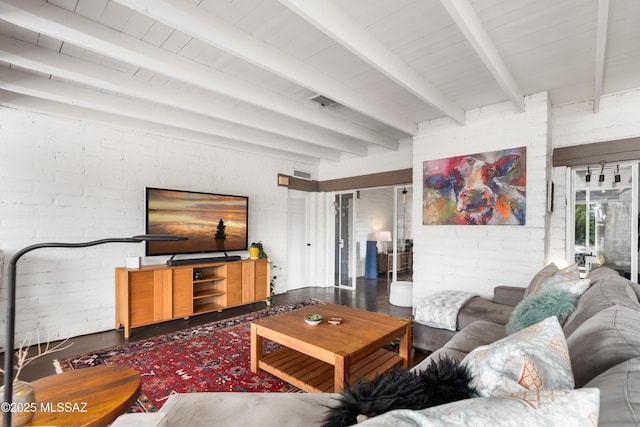 living room featuring beamed ceiling and brick wall