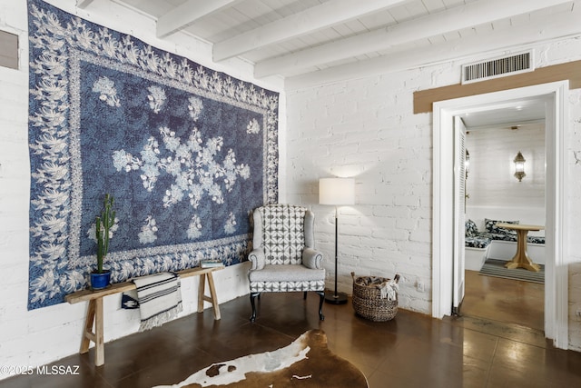 sitting room featuring beam ceiling and brick wall