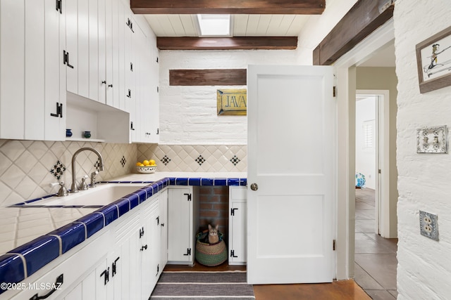 kitchen with sink, backsplash, tile countertops, and white cabinets