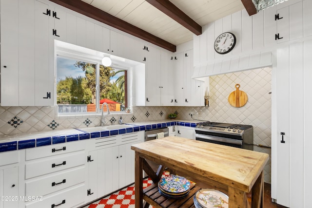 kitchen featuring beamed ceiling, sink, white cabinets, tile counters, and stainless steel appliances