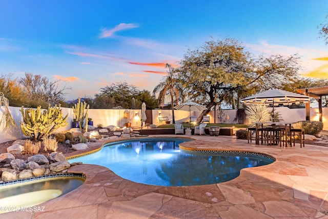 pool at dusk featuring a patio and an in ground hot tub