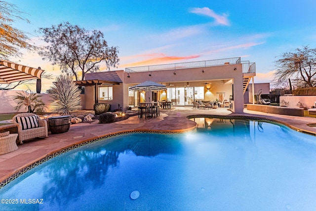 pool at dusk with ceiling fan and a patio