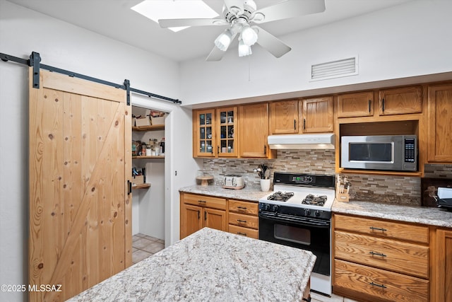 kitchen featuring tasteful backsplash, a barn door, ceiling fan, and gas range oven