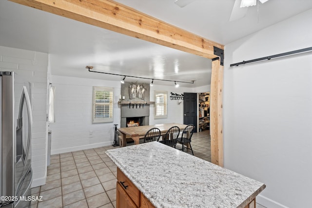 kitchen with ceiling fan, a fireplace, a kitchen island, light tile patterned flooring, and stainless steel fridge