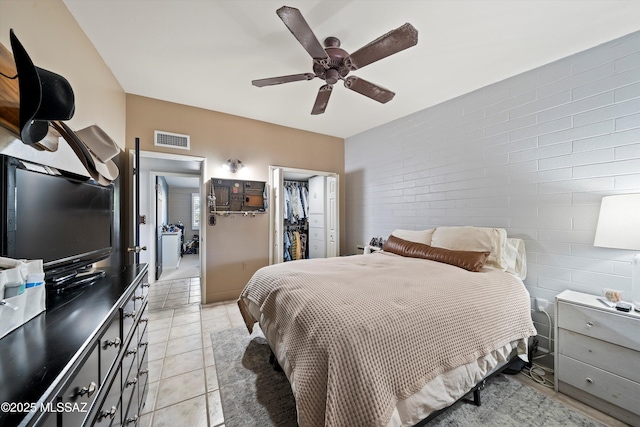 tiled bedroom with ceiling fan, a walk in closet, a closet, and brick wall