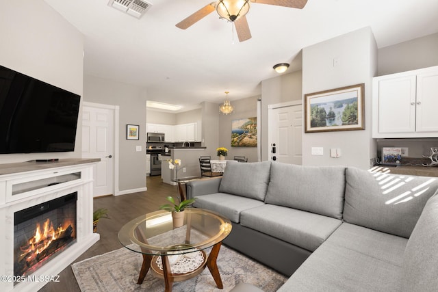 living room with ceiling fan with notable chandelier, dark hardwood / wood-style flooring, and a premium fireplace