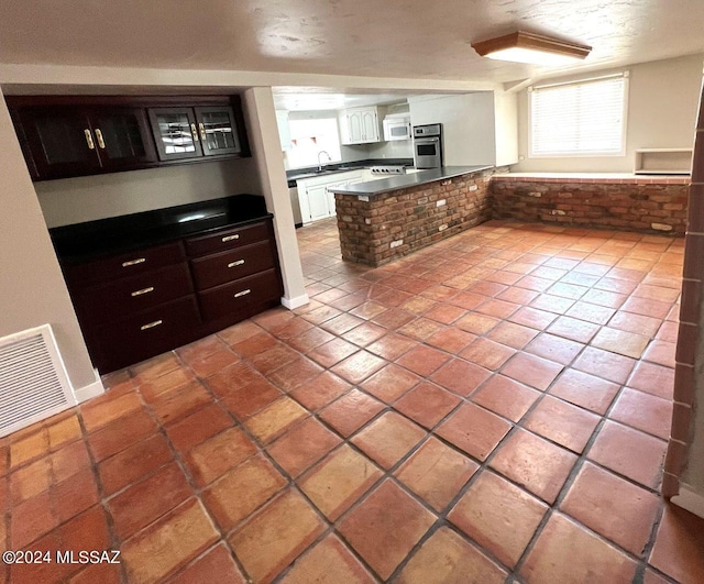 kitchen featuring kitchen peninsula, white cabinetry, appliances with stainless steel finishes, light tile patterned flooring, and sink