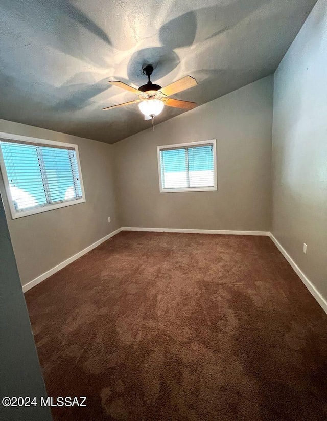 empty room featuring a textured ceiling, ceiling fan, vaulted ceiling, and dark colored carpet