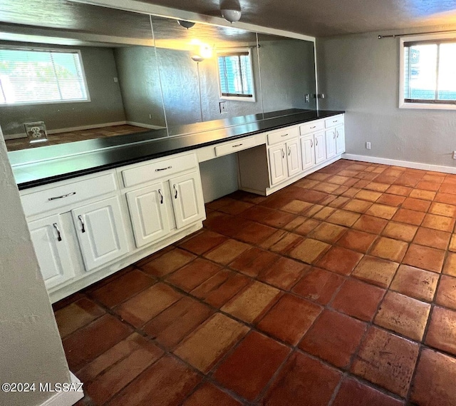 kitchen with built in desk, dark tile patterned flooring, and white cabinetry