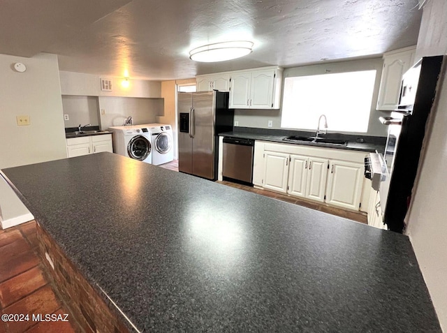 kitchen with appliances with stainless steel finishes, white cabinetry, washing machine and dryer, and sink