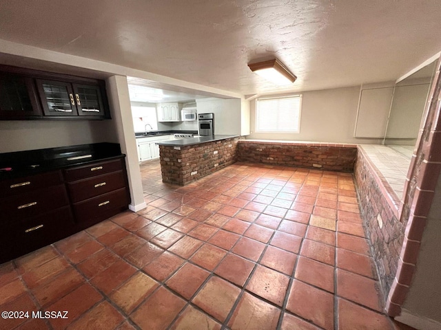 kitchen with oven, white cabinets, a textured ceiling, kitchen peninsula, and dark brown cabinetry