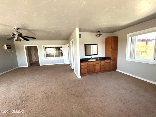 unfurnished living room featuring an AC wall unit, carpet floors, ceiling fan, a textured ceiling, and sink