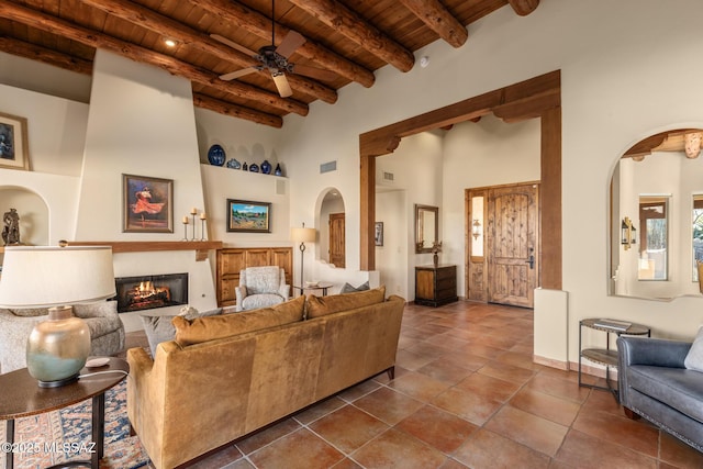 tiled living room featuring ceiling fan, beam ceiling, a towering ceiling, a large fireplace, and wooden ceiling